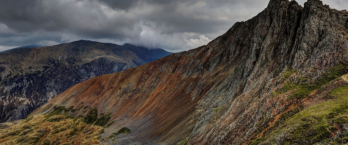 A rugged mountain landscape with steep cliffs and a cloudy sky.