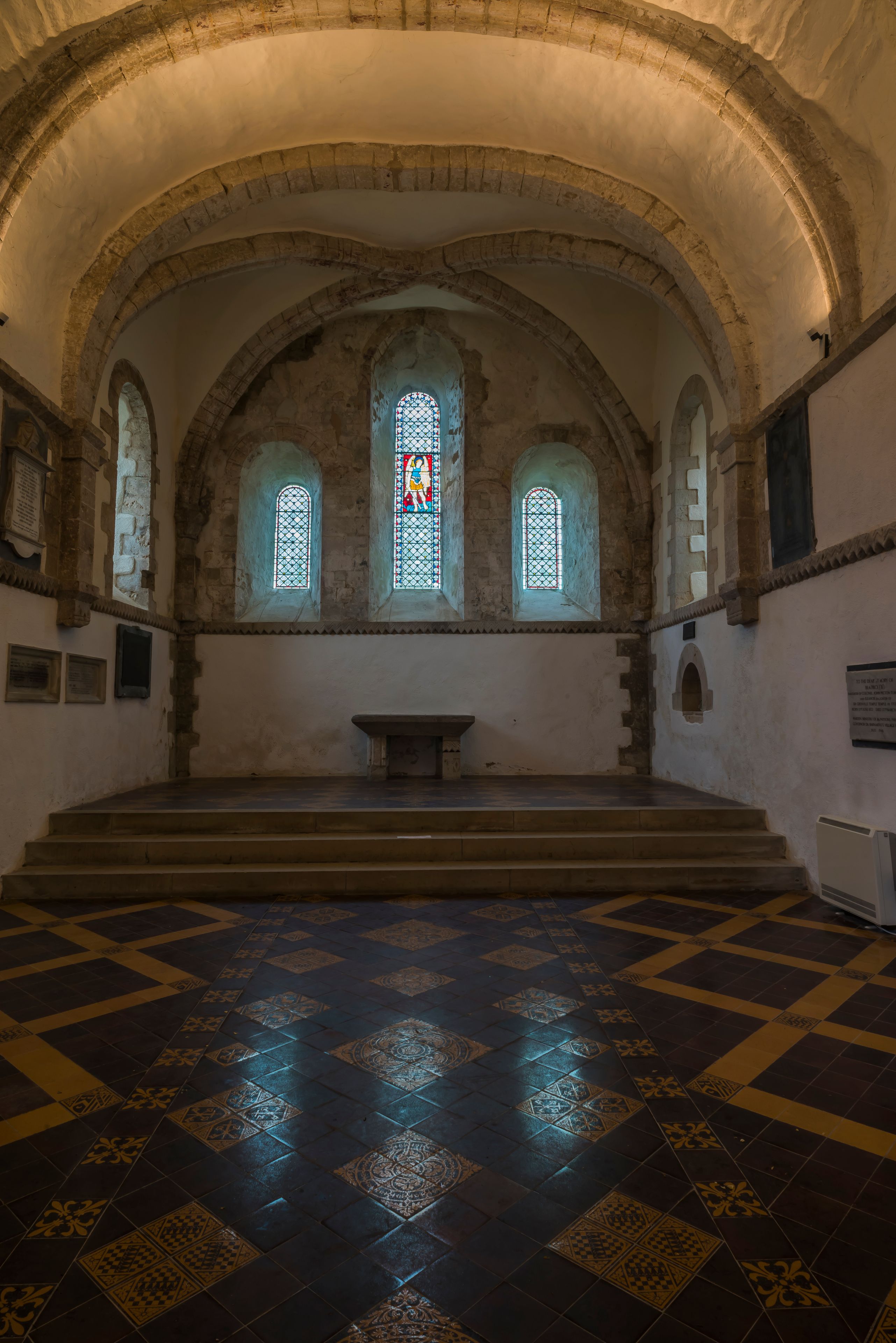 Interior de iglesia con techos abovedados, vidrieras de colores y baldosas de suelo con diseño.