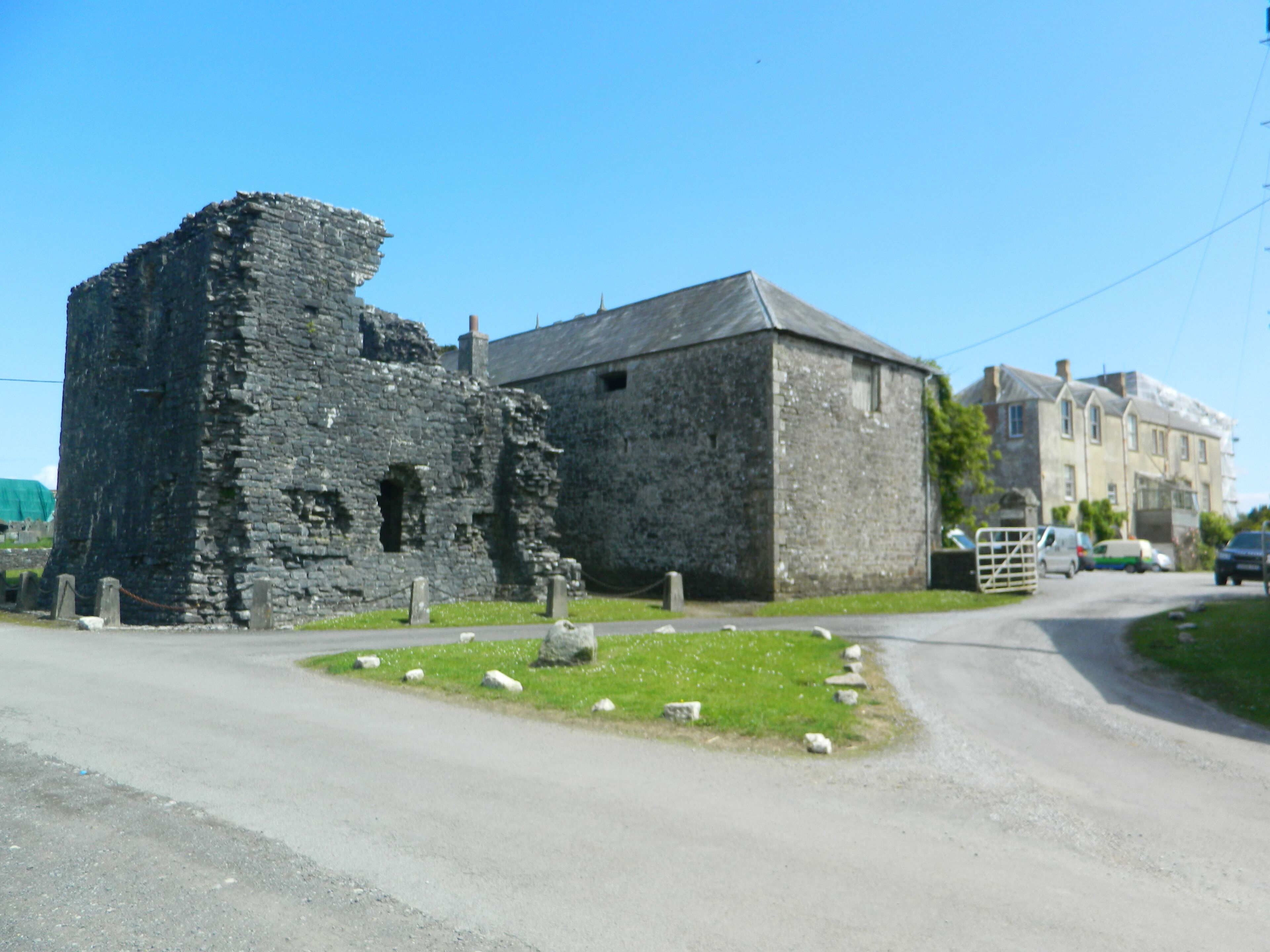 A stone building with a large tower, a smaller adjacent building, and a grassy area with sheep.