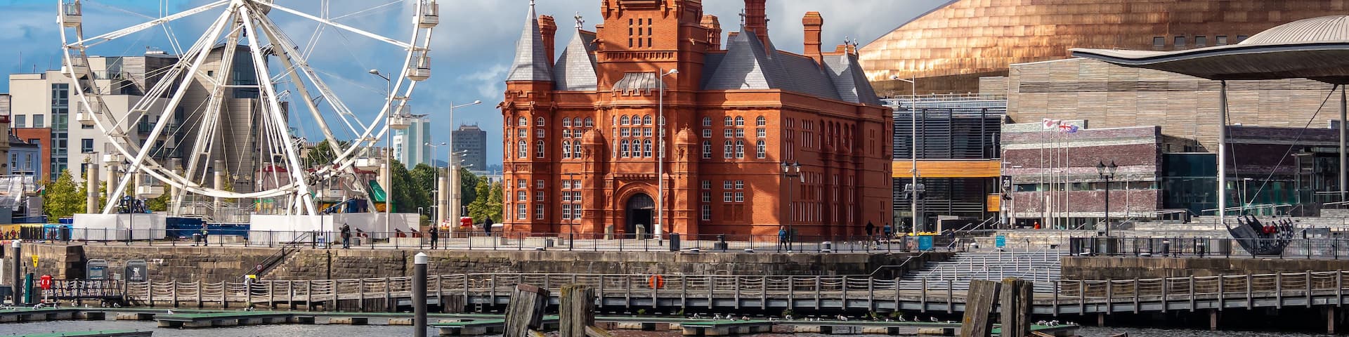 A historic red brick building with a clock tower, a large white Ferris wheel, and a modern stadium.