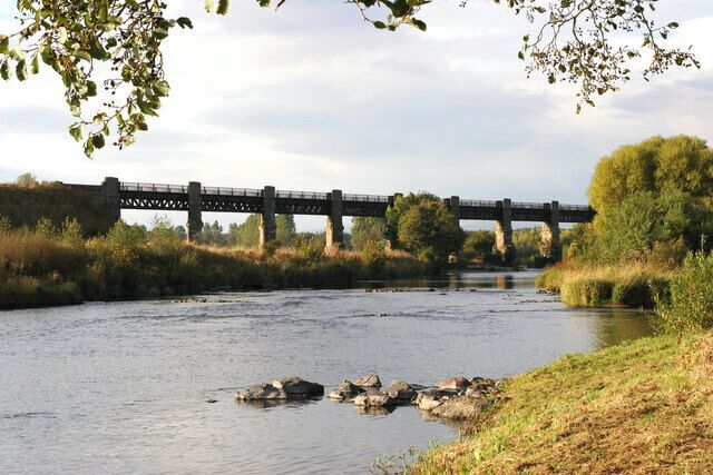 A river with a bridge, surrounded by trees and grassy banks.