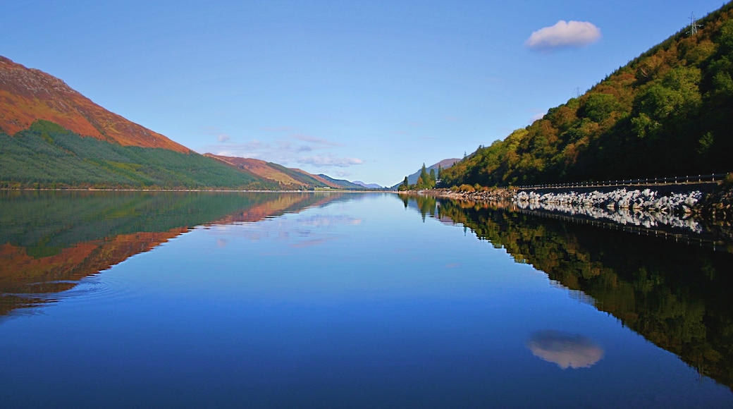 A calm river reflecting the surrounding mountains and clear sky.