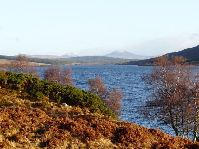 A lake surrounded by hills and sparse vegetation.