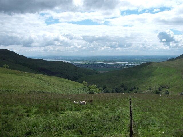 A green valley with rolling hills and a distant view of a body of water.