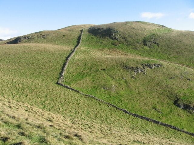A grassy hill with a stone wall running down its center.