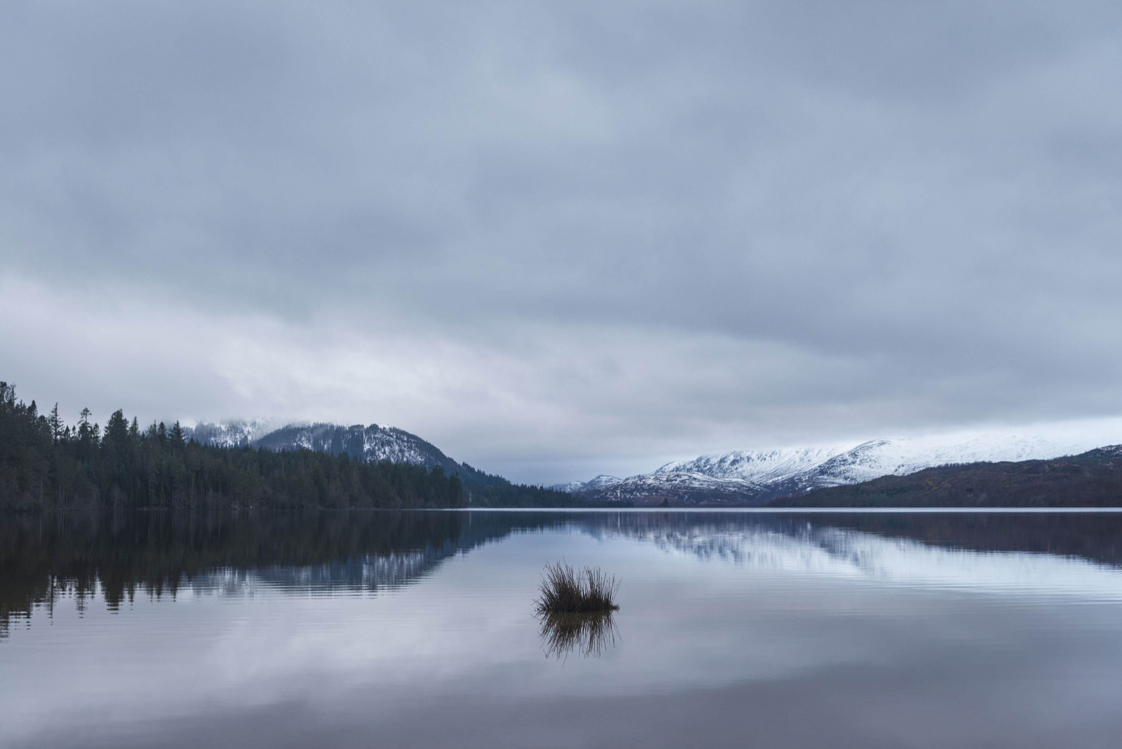 A calm lake with a reflection of the surrounding mountains and trees.