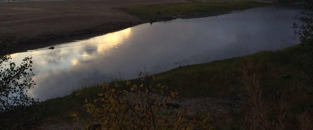 A river reflecting the sky, surrounded by grassy banks and distant mountains.