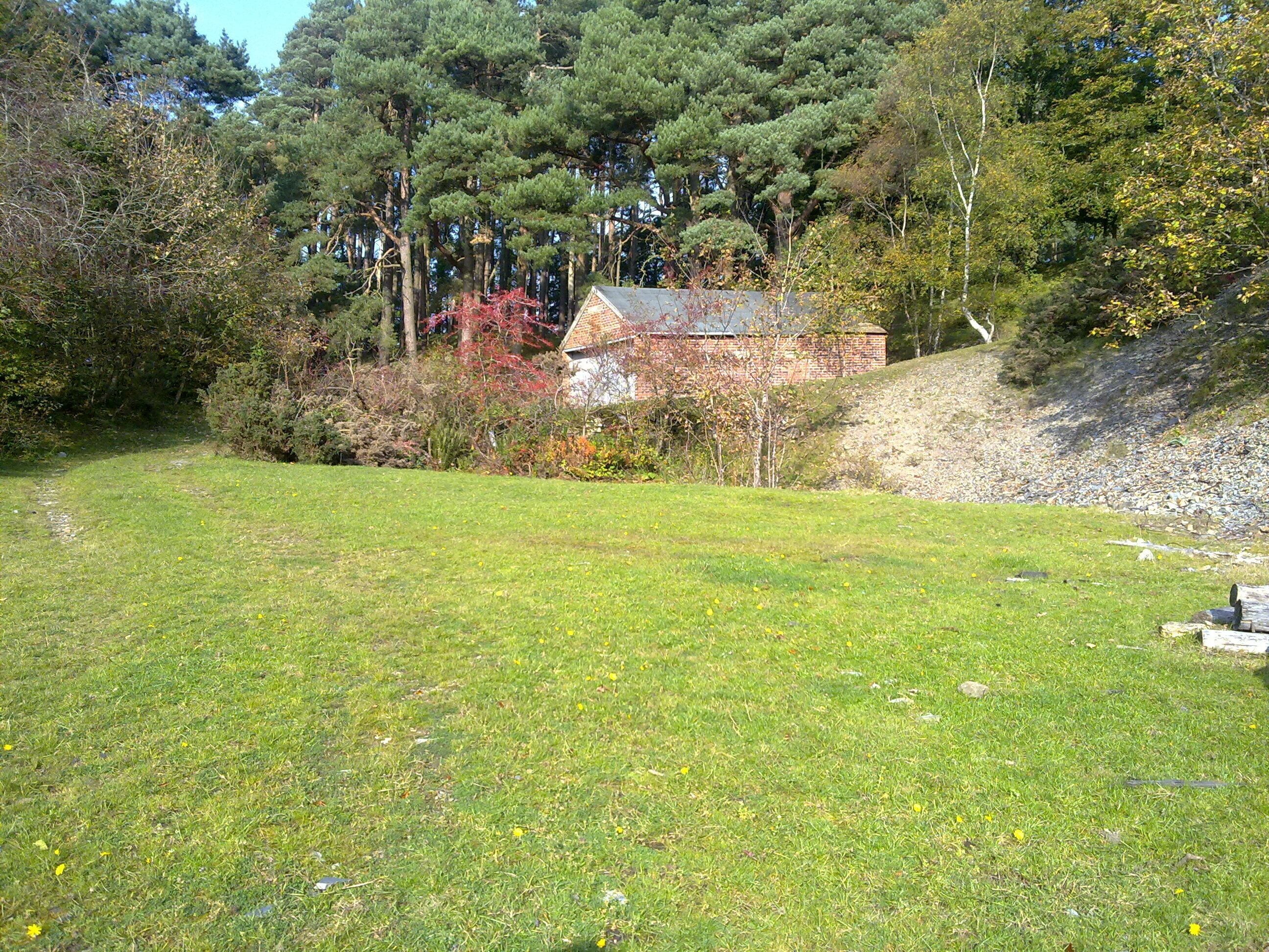 A grassy field with a stone wall, trees, and a building with a red roof.