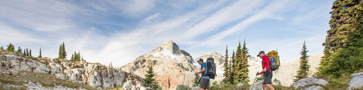 Side view and reflection of backpackers hiking beside alpine lake.
