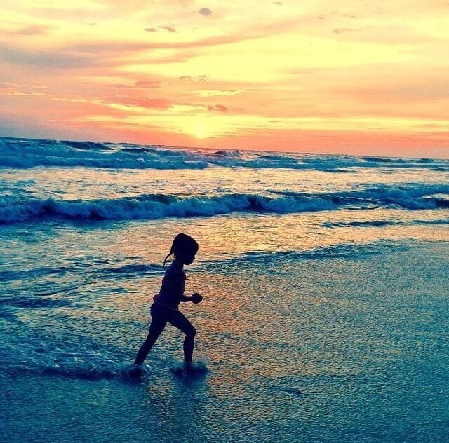 A silhouette of a child playing in the water at sunset.