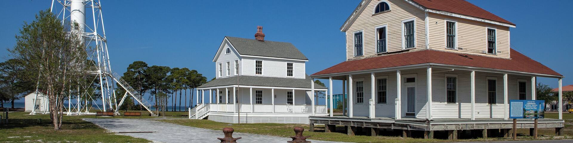 A lighthouse, a white house with a red roof, and another white house with a grey roof.