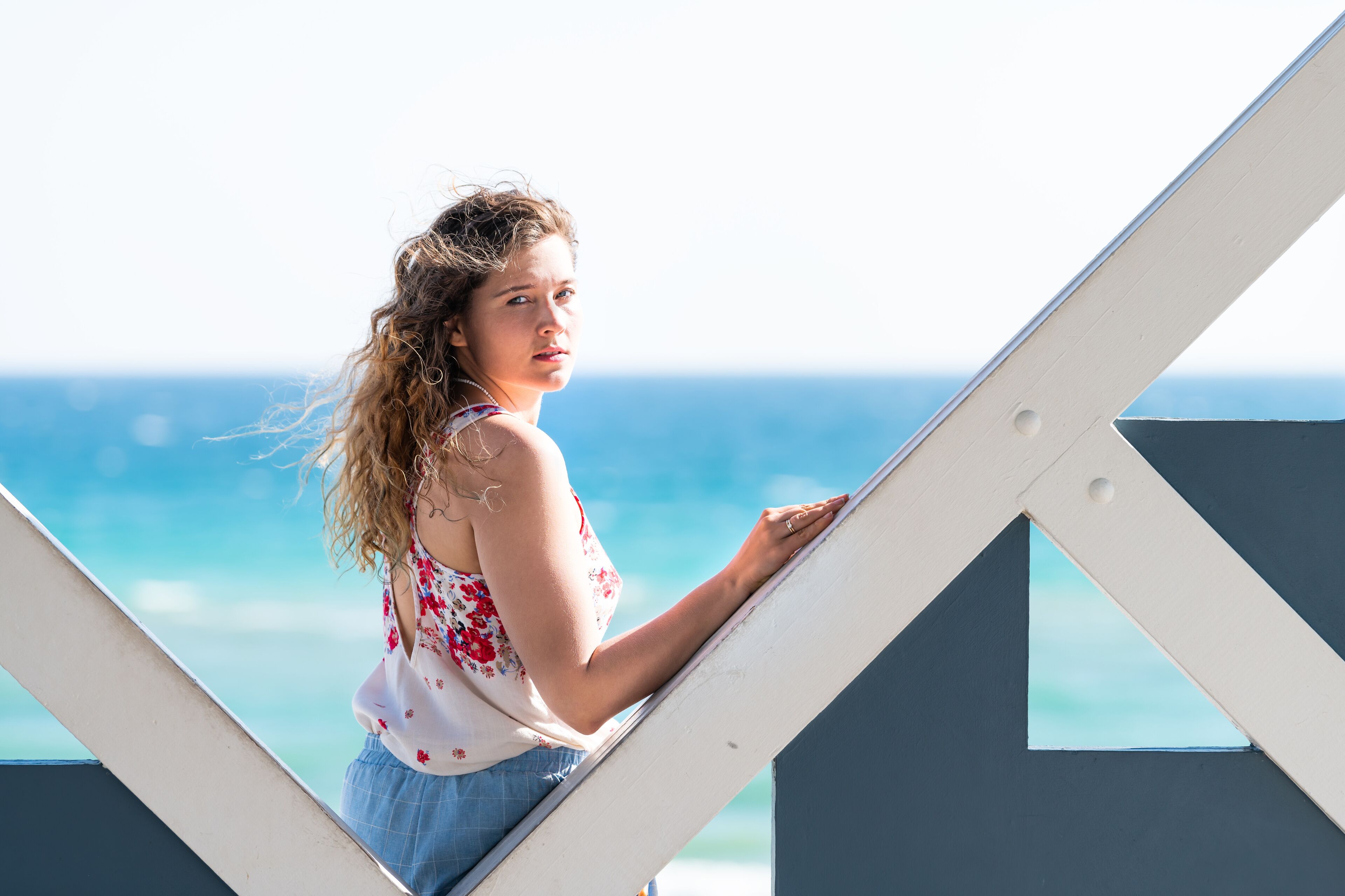 A person leaning on a white structure with a view of the ocean.