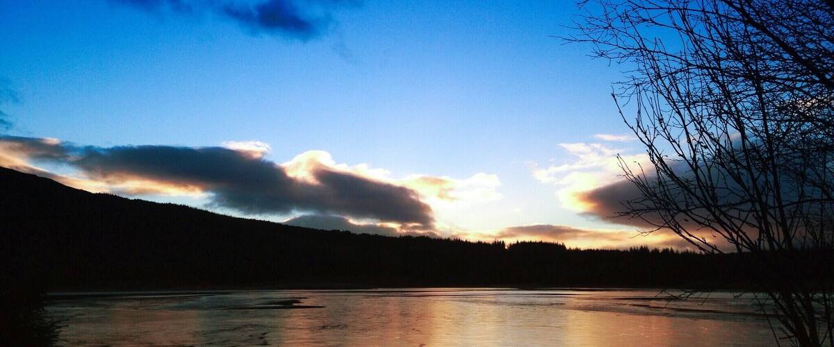 A frozen lake with reflections of the sky, surrounded by trees and hills.