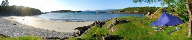 A beach with a tent, rocky shoreline, and calm water.