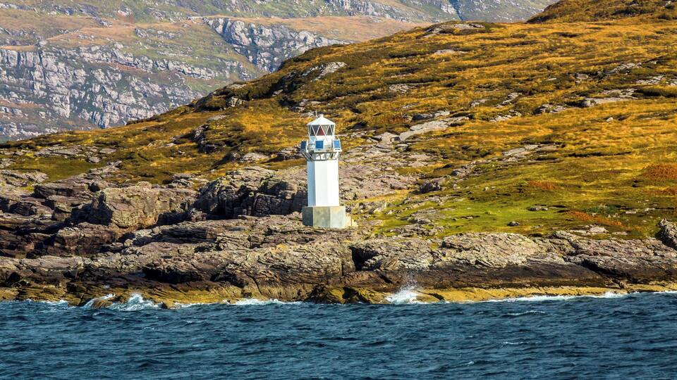 A lighthouse on a rocky coastline with a mountainous backdrop.