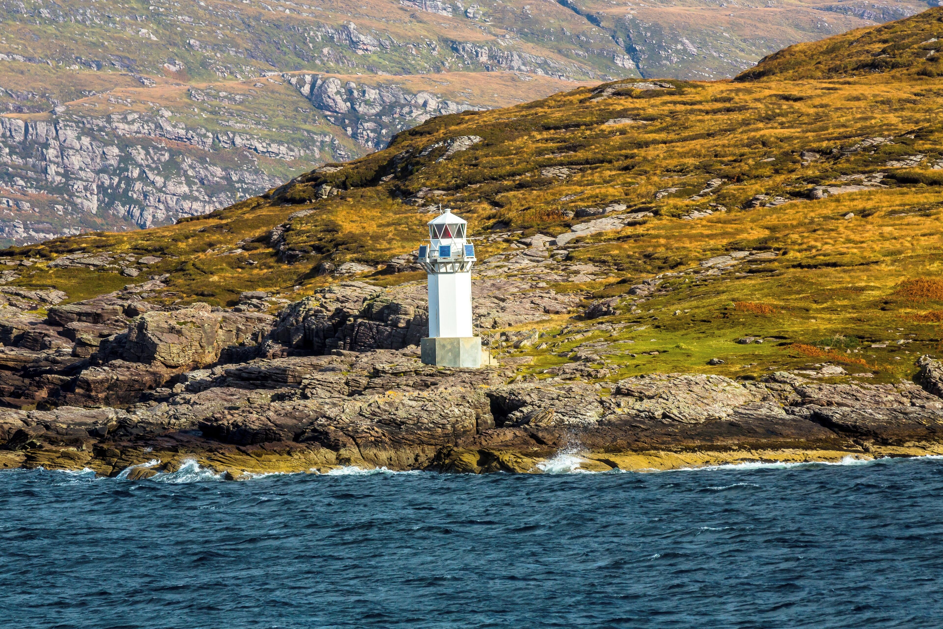 A lighthouse on a rocky coastline with a mountainous backdrop.
