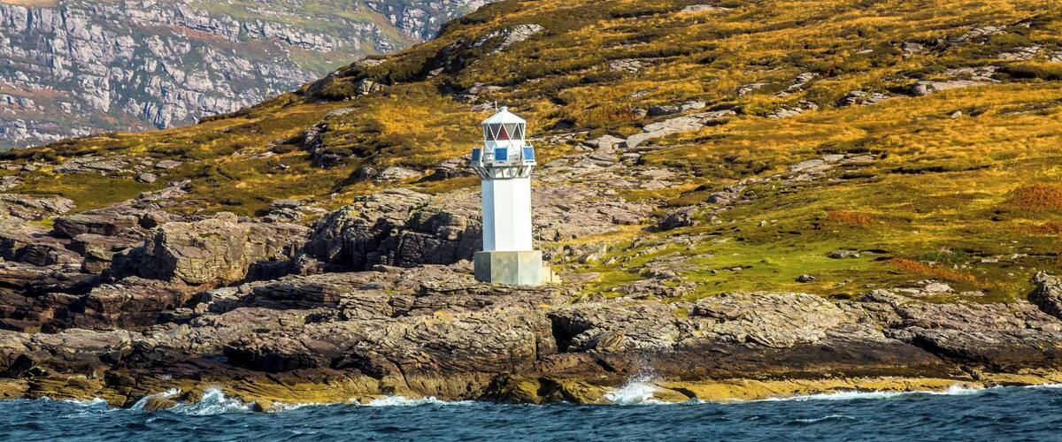 A lighthouse on a rocky coastline with a mountainous backdrop.