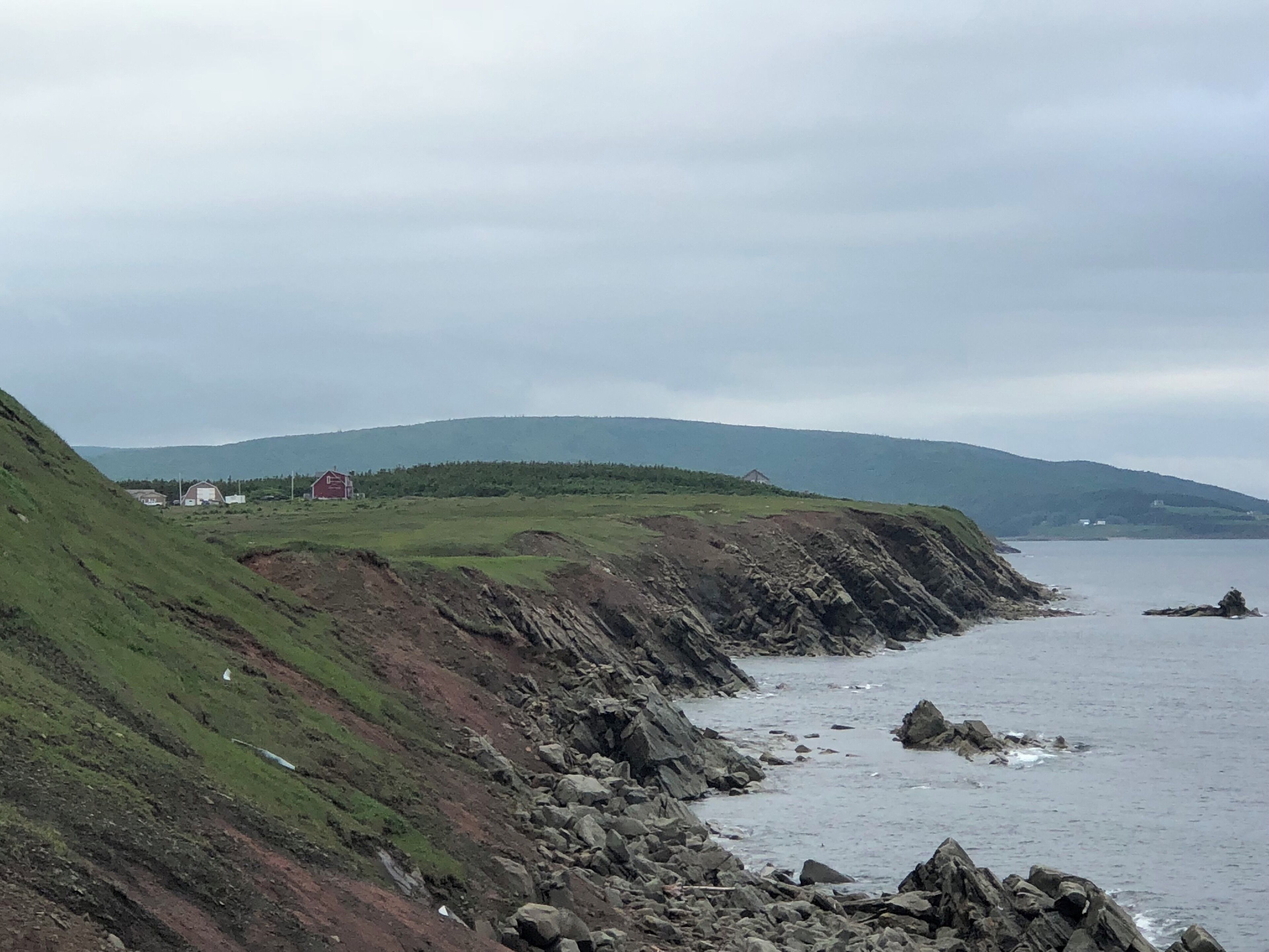 A coastal landscape with rocky cliffs, grassy slopes, and a distant view of a red building.