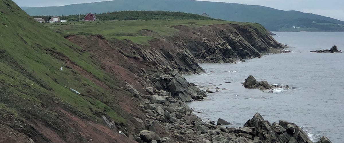 A coastal landscape with rocky cliffs, grassy slopes, and a distant view of a red building.