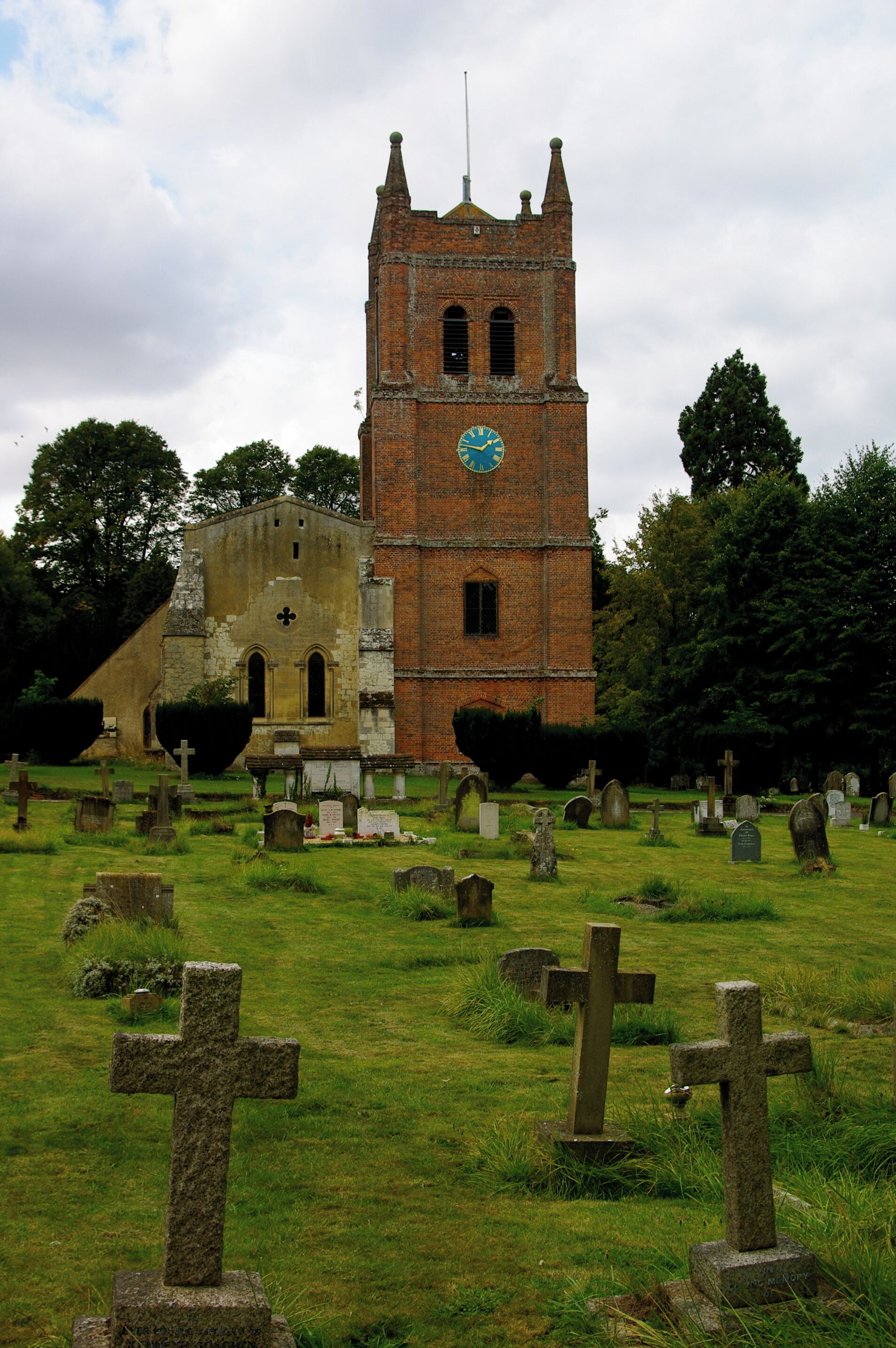 A church with a clock tower and a cemetery with numerous gravestones.