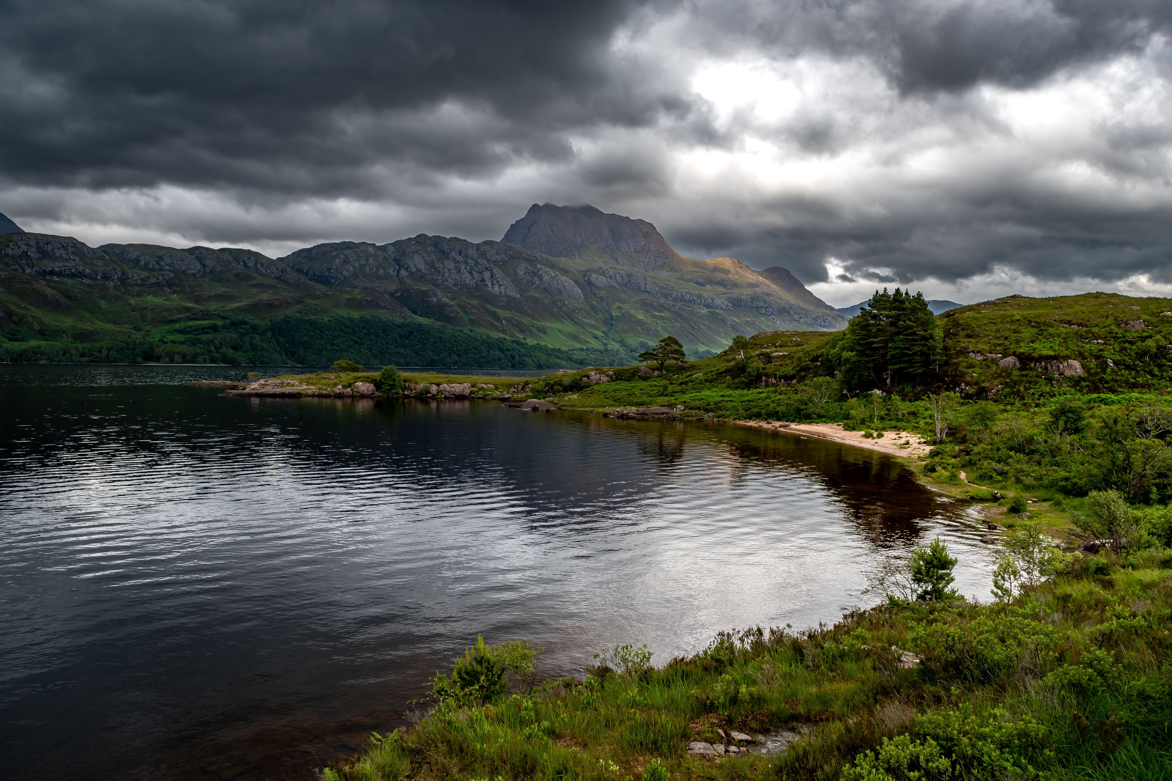 A lake surrounded by mountains under a cloudy sky.