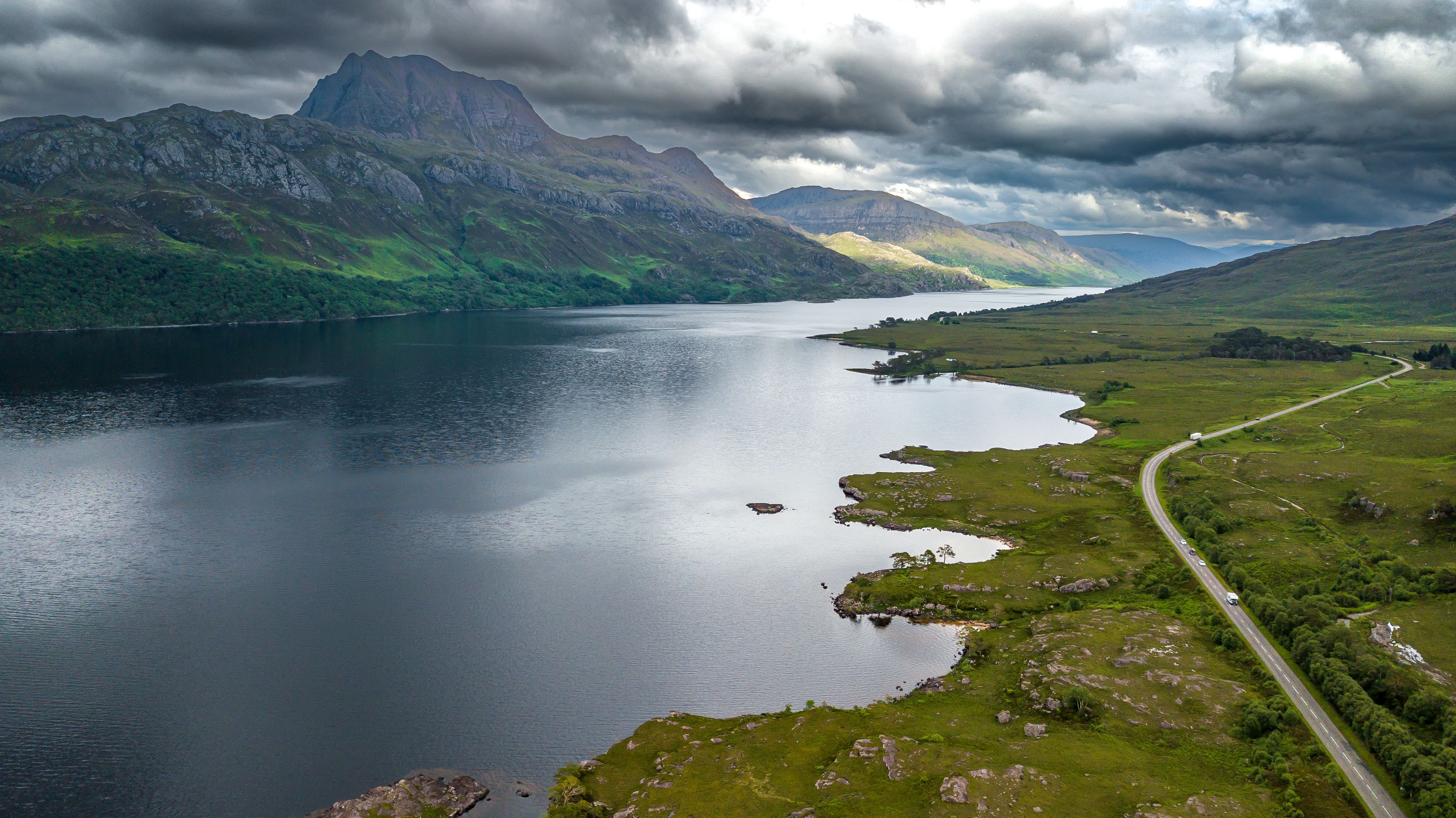 A lake surrounded by mountains, a winding road, and a cloudy sky.