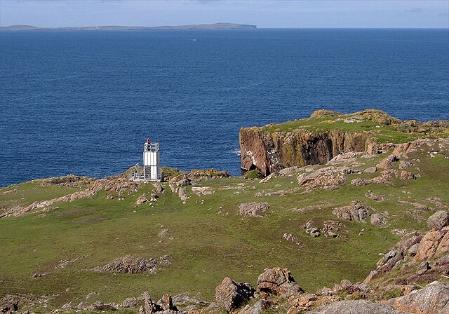 A lighthouse on a grassy cliff by the sea.