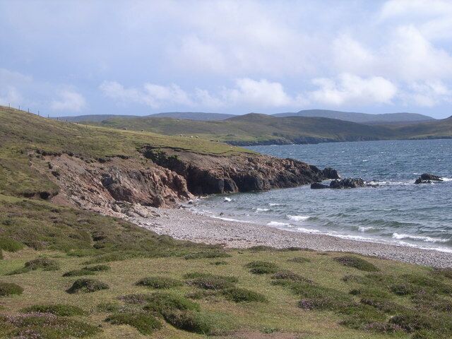 Un paisaje costero con colinas cubiertas de hierba, una costa rocosa y un mar tranquilo.