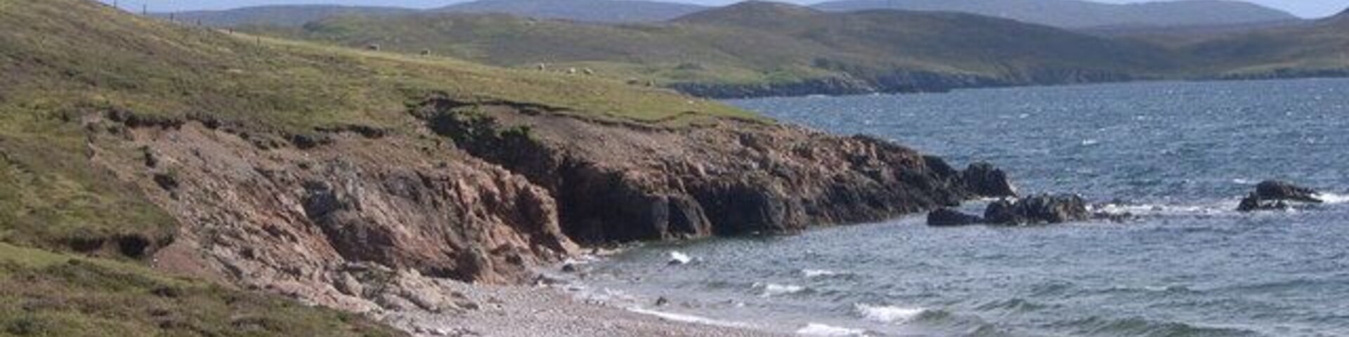 Un paisaje costero con colinas cubiertas de hierba, una costa rocosa y un mar tranquilo.
