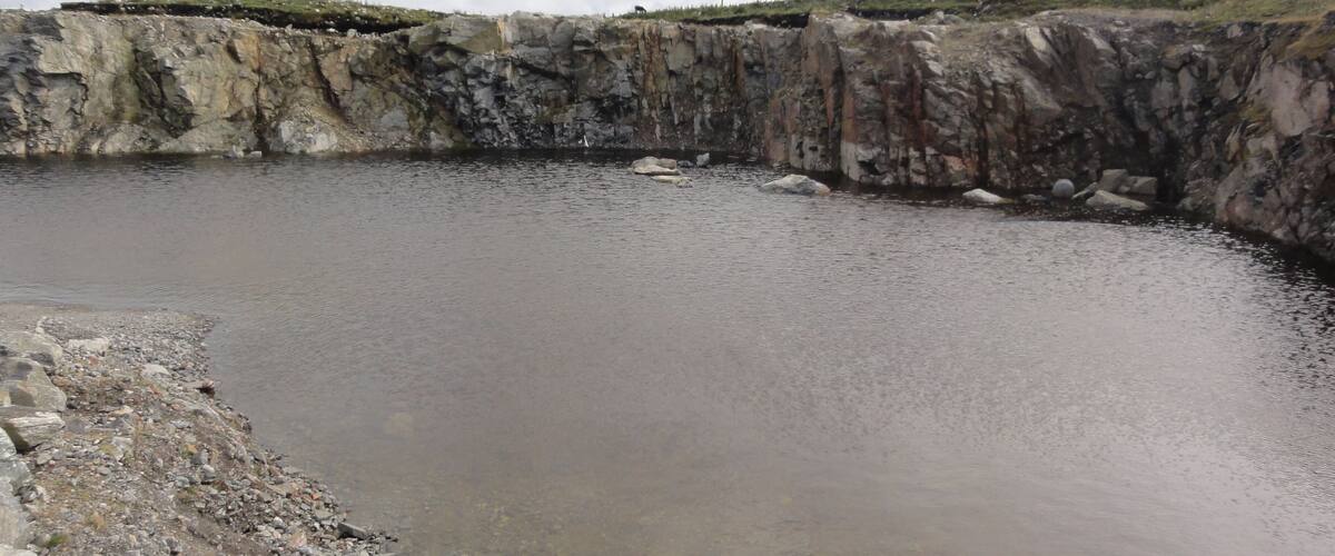 A large, circular pond surrounded by rocky terrain and sparse vegetation.