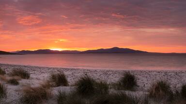 A beach with sand dunes and a sunset over the water.