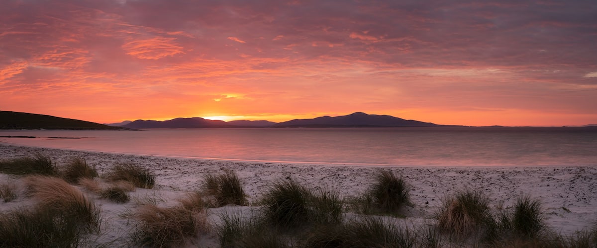 A beach with sand dunes and a sunset over the water.