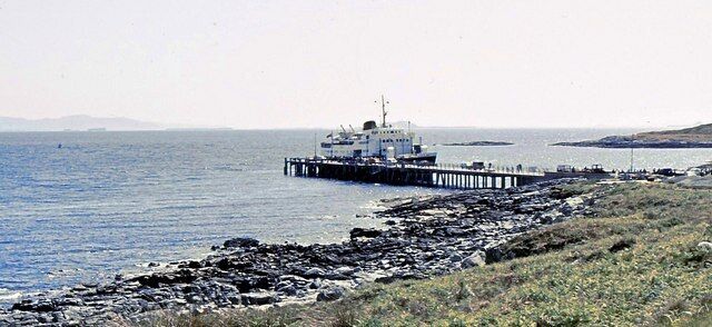 A rocky shoreline with a pier extending into the water, a boat docked at the pier, and distant landforms.