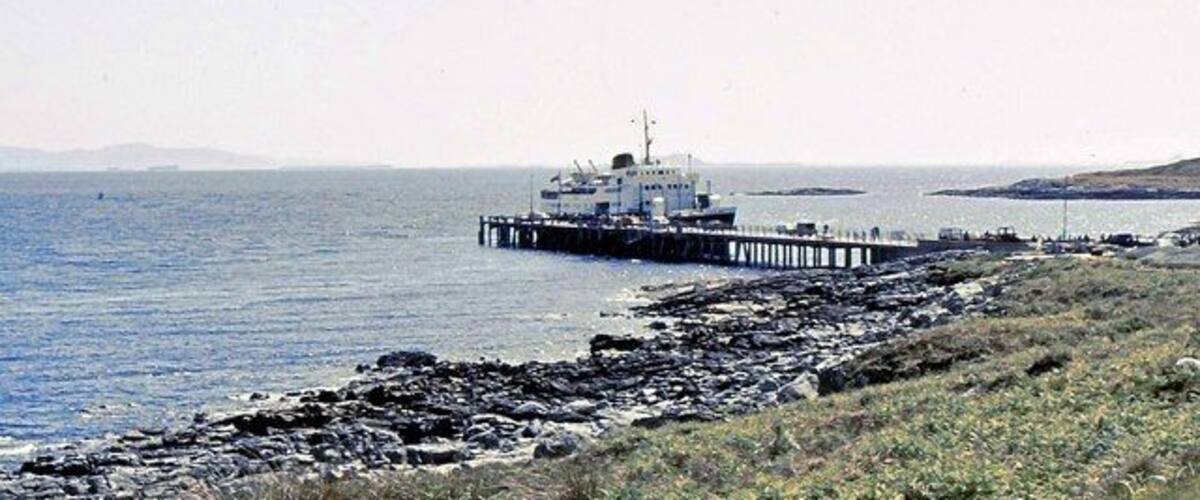 A rocky shoreline with a pier extending into the water, a boat docked at the pier, and distant landforms.