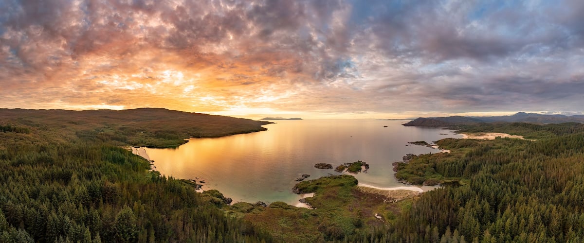 A lake surrounded by dense forests and hills during sunset.