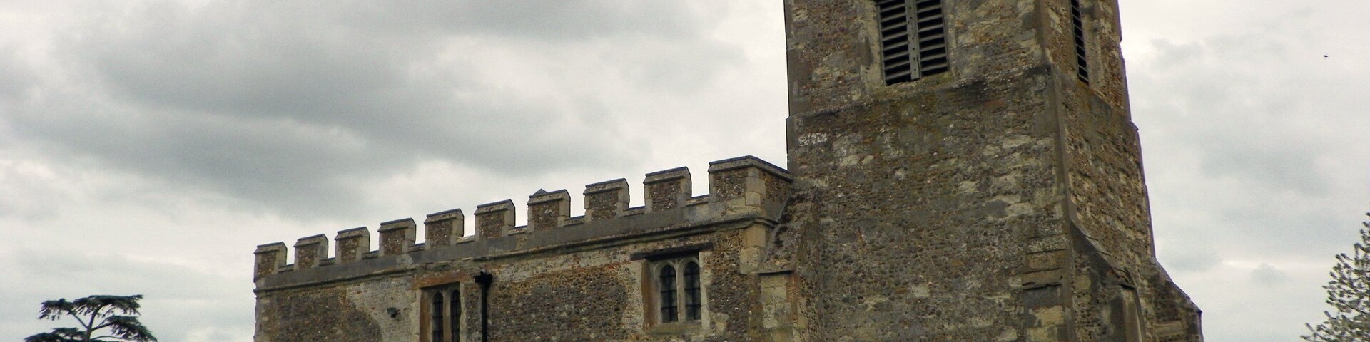 Uma igreja de pedra histórica com uma alta torre de sino e janelas em arco.