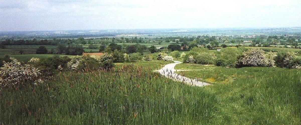 A grassy hillside with a winding path leading to a distant view of a valley.