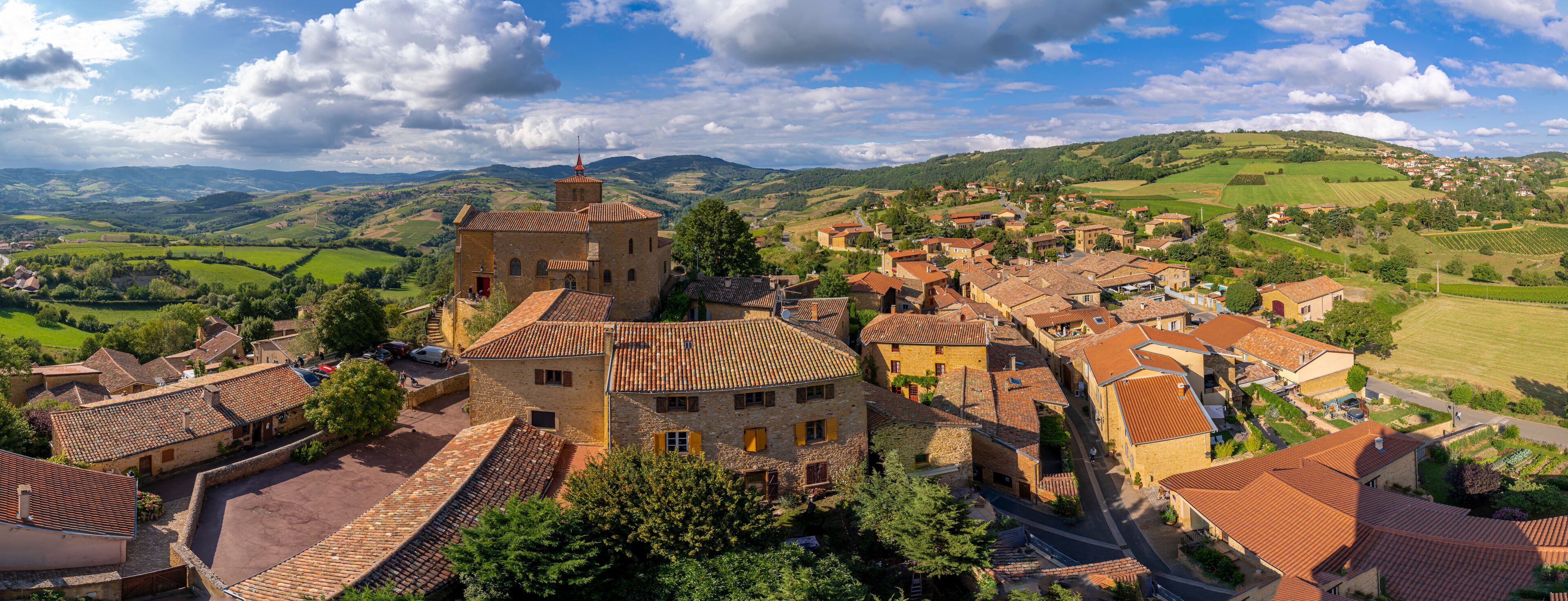A historic village with stone buildings, a prominent tower, and rolling hills in the background.