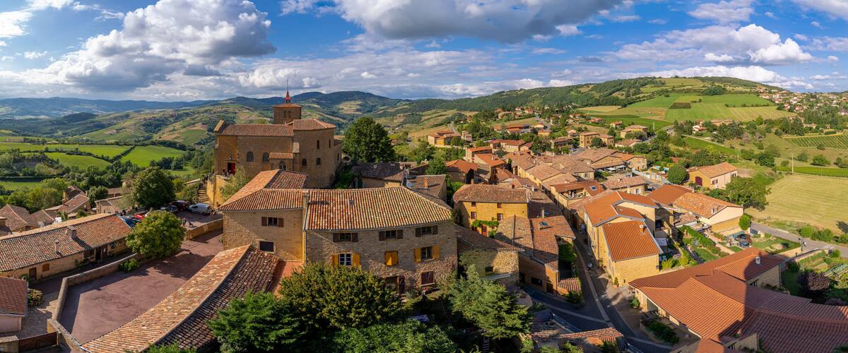 A historic village with stone buildings, a prominent tower, and rolling hills in the background.