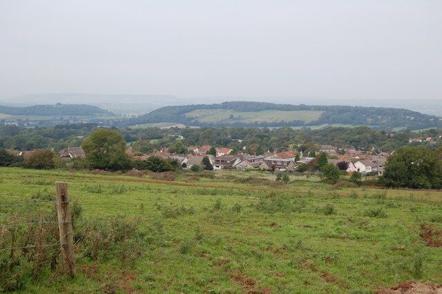 A rural landscape with rolling hills, scattered houses, and a wooden fence in the foreground.
