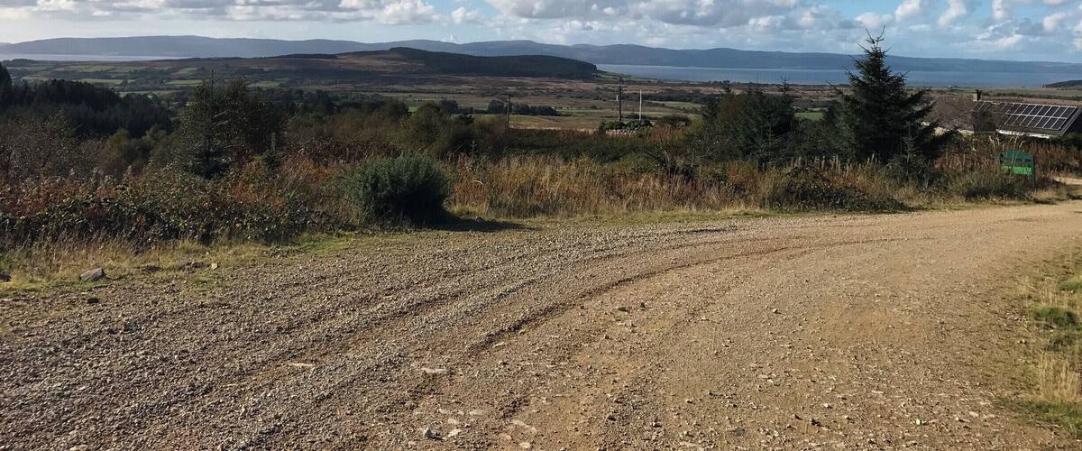 A gravel path leading through a rural landscape with rolling hills and a body of water in the distance.