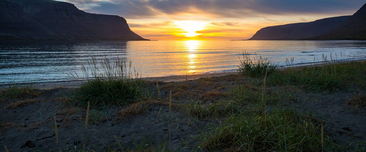 A sunset over a calm river with grassy banks and cliffs on either side.