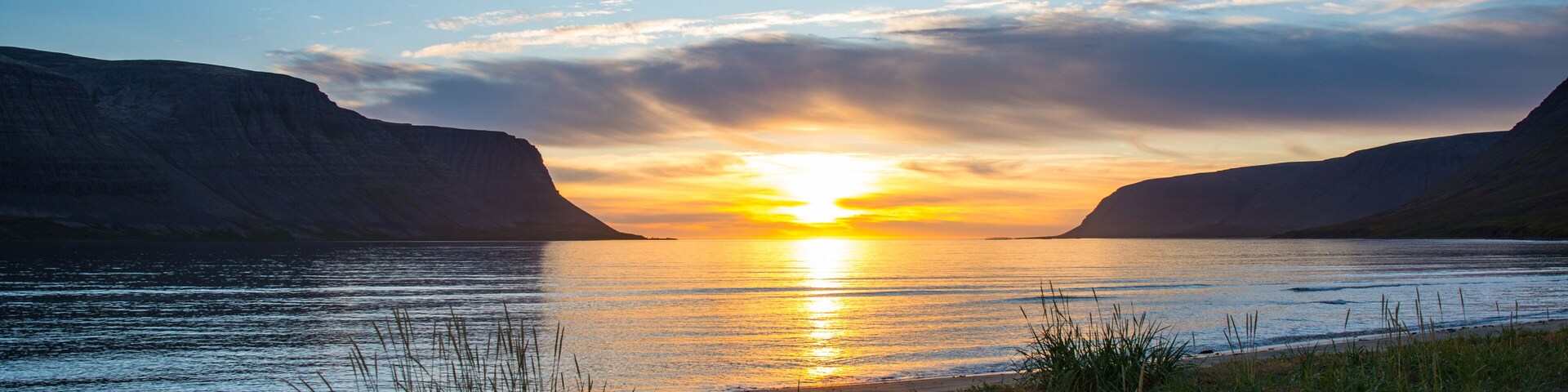 A sunset over a calm river with grassy banks and cliffs on either side.