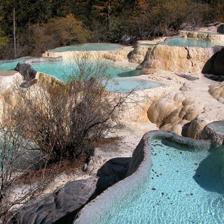 Terraced pools with clear turquoise water, surrounded by rocky formations and sparse vegetation.