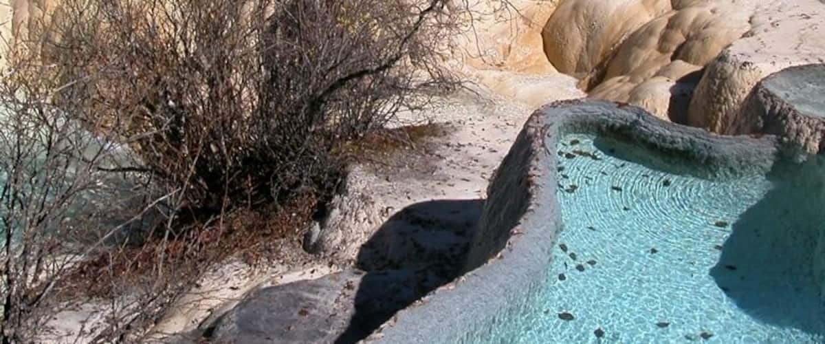 Terraced pools with clear turquoise water, surrounded by rocky formations and sparse vegetation.