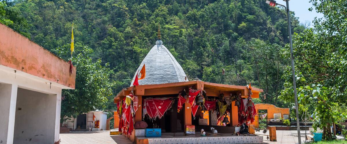 A temple with a conical roof, surrounded by lush greenery and a mountain in the background.