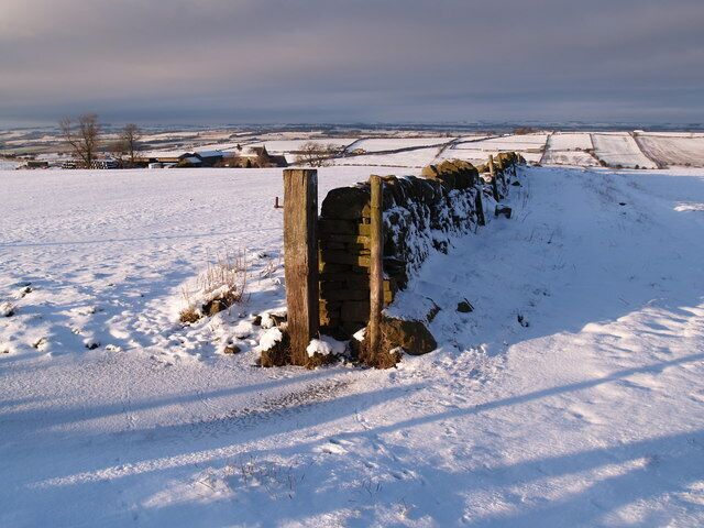 A snow-covered landscape with a stone wall and a wooden post.