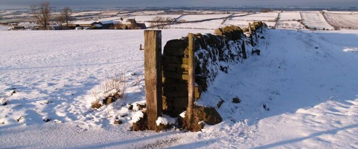 A snow-covered landscape with a stone wall and a wooden post.