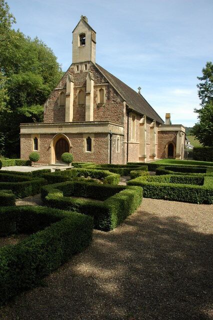 A church with a bell tower, surrounded by a formal garden with hedges and a gravel path.