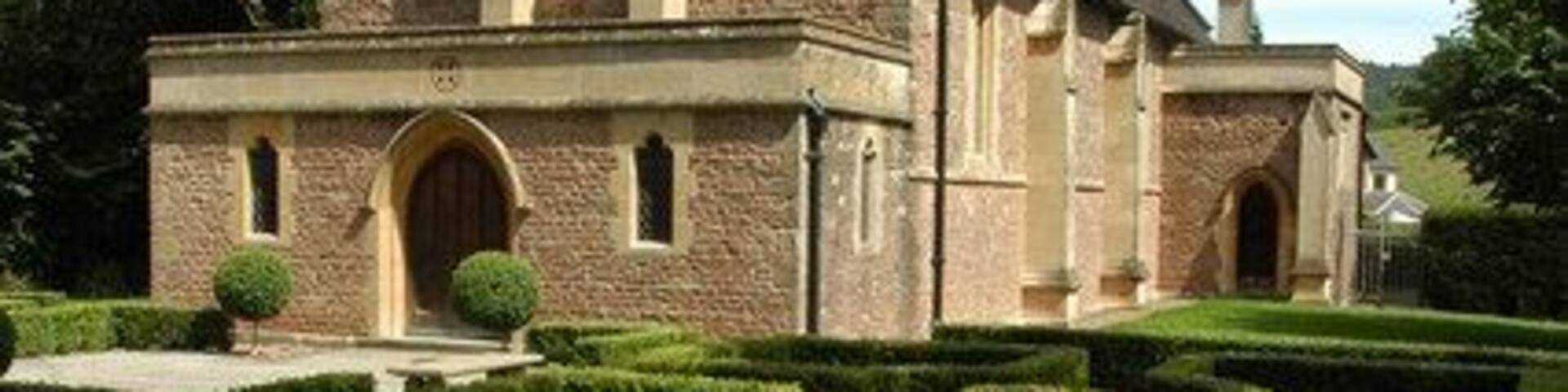 A church with a bell tower, surrounded by a formal garden with hedges and a gravel path.